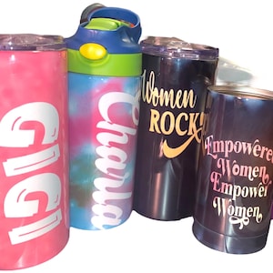 May include: Four stainless steel tumblers with various designs. One pink tumbler with the name "Gigi" in white lettering, one blue tumbler with the name "Charla" in white lettering, one black tumbler with the text "Women Rock" in gold lettering, and one purple tumbler with the text "Empowered Women Empower Women" in pink lettering.