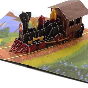 May include: A 3D pop-up card depicting a black and red steam train on a track. The card has a brown roof and yellow details. The background shows a landscape with trees, a lake, and a field of flowers.