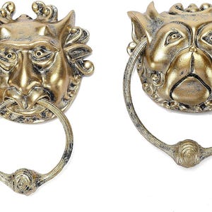May include: Two gold-toned door knockers with animal faces. One knocker features a bull's head with horns and the other features a dog's head with floppy ears.