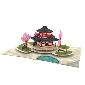 May include: A pop-up card depicting a Japanese pagoda with a red and black roof, set in a garden with pink cherry blossom trees and a pond with koi carp. The card is on a light beige background.