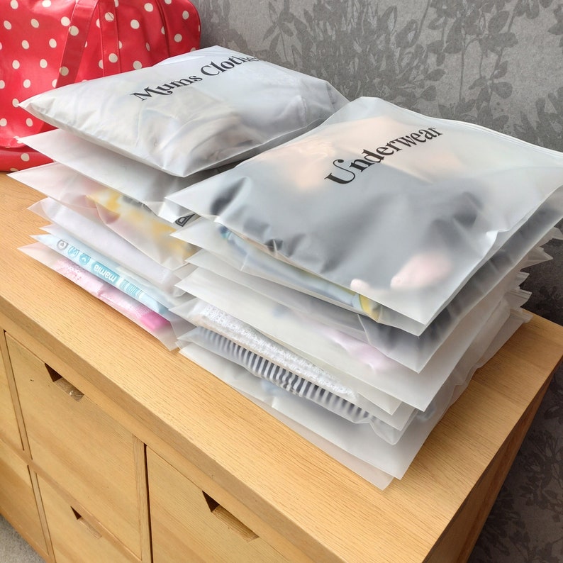 Może przedstawiać: Stos przezroczystych plastikowych toreb do przechowywania z zamkami błyskawicznymi. Torby są oznaczone napisami "Mums Cloth" i "Underwear".