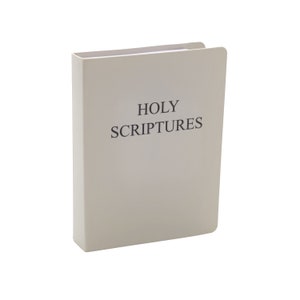 Puede incluir: Un libro blanco con el título "HOLY SCRIPTURES" impreso en negro.