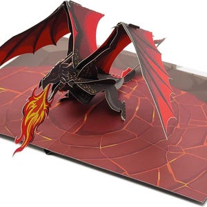 May include: A pop-up card depicting a black dragon with red wings and flames. The dragon is above a red and brown landscape with a cracked pattern. The card is open, revealing the three-dimensional design.