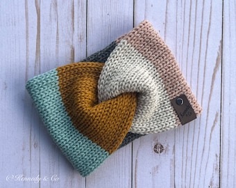 May include: A knitted headband with a twisted design in shades of teal, mustard yellow, cream, and blush pink. The headband has a brown leather tag with the text "Kennedy & Co."