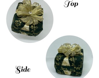 May include: A square, decorative ornament in the shape of a gift box. The box is dark green with a floral pattern and a gold ribbon with a crystal accent. The ornament is designed to be hung.