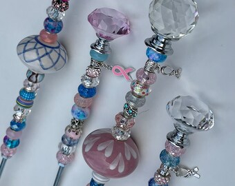 May include: Four decorative garden stakes with crystal tops and colorful beads. The stakes feature pink and blue beads, a pink ribbon charm, and a charm with the word "HOPE".