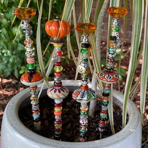 May include: Four decorative garden stakes with a Halloween theme. Each stake features a variety of colorful beads, charms, and a ceramic pumpkin or mushroom top.