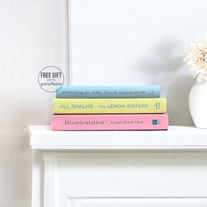 May include: A stack of three books on a white shelf. The top book is light blue with the title "THE TECH SOLUTION" by Shimi Kang. The middle book is yellow with the title "The LEMON SISTERS" by Jill Shalvis. The bottom book is pink with the title "Disorientation" by Elaine Hsich Chou.