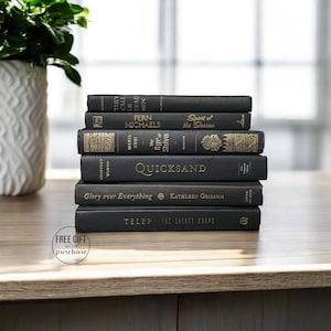 May include: A stack of eight black hardcover books with gold lettering on the spines. The titles include "They Call Us Dead Men", "Fern Michaels", "Spirit of the Season", "The Rip of Shiva", "Quicksand", "Glory over Everything", "Kathleen Grissom", and "The Secret Corps".