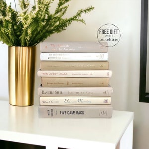 May include: A stack of ten books with beige covers, featuring titles like "The Midwife and the Assassin", "The Lucky Years", "Bread and Butter", "Prodigal Son", "Elvis in the Morning", and "Five Came Back". The books are stacked on a white surface with a gold vase and a green plant in the background. The text "FREE GIFT WITH purchase" is visible in a circle at the top of the image.