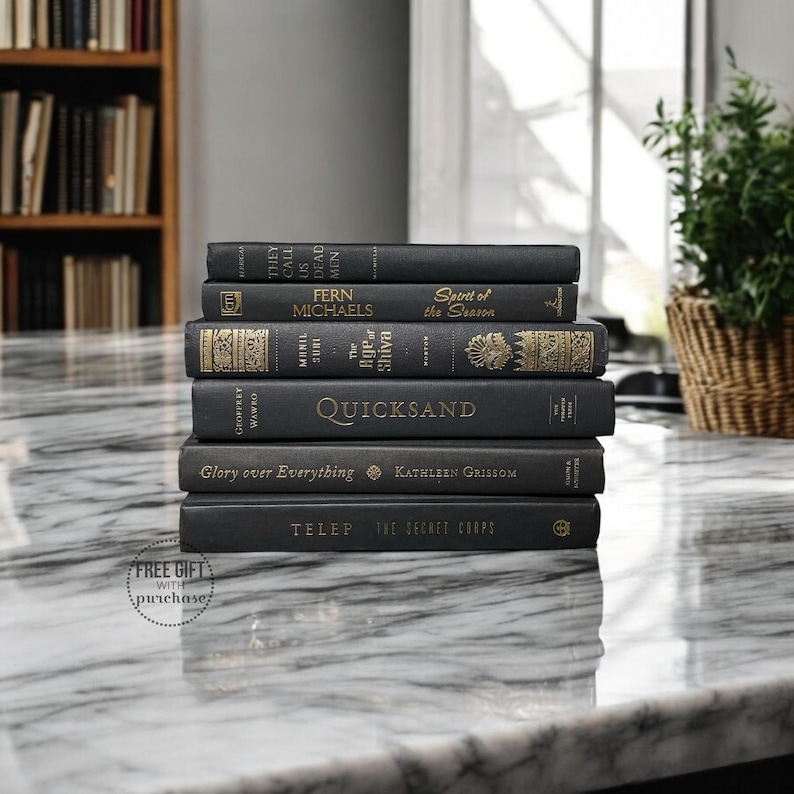 May include: A stack of black hardcover books with gold lettering on a white marble surface. The titles include "They Call Us Dead Men", "Spirit of the Season", "The Rise of Shiva", "Quicksand", "Glory over Everything", and "The Secret Corps".