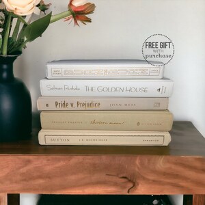 May include: A stack of five books with white, beige, and green covers. The top book has the title "Burn for Burn" and the author "Han/Vivian". The second book has the title "The Golden House" and the author "Salman Rushdie". The third book has the title "Pride v. Prejudice" and the author "Joan Hess". The fourth book has the title "thirteen moons!" and the author "Charles Frazier". The bottom book has the title "Sutton" and the author "J.R. Moehringer".