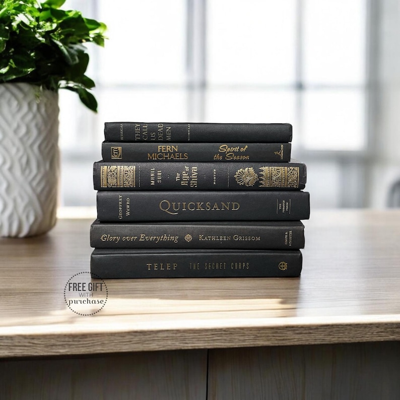 May include: A stack of eight black hardcover books with gold lettering on the spines. The titles include "They Call Us Dead Men", "Fern Michaels", "Spirit of the Season", "The Rip of Shiva", "Quicksand", "Glory over Everything", "Kathleen Grissom", and "The Secret Corps".