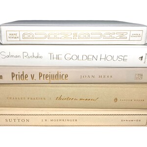May include: A stack of five books with white and beige covers. The titles are "Burn for Burn", "The Golden House", "Pride v. Prejudice", "Thirteen Moons", and "Sutton".
