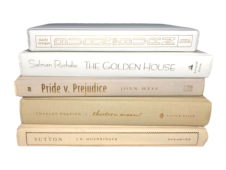 May include: A stack of five books with white and beige covers. The titles are "Burn for Burn", "The Golden House", "Pride v. Prejudice", "Thirteen Moons", and "Sutton".