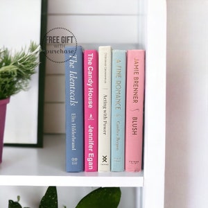 May include: A bookshelf with a variety of books, including "The Identicals" by Elin Hilderbrand, "The Candy House" by Jennifer Egan, "Acting with Power" by Deborah Gruenfeld, "A Fine Romance" by Candice Bergen, and "Jamie Brenner's Blush".