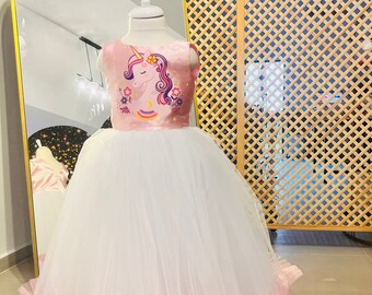 May include: A white tulle dress with a pink bodice featuring a unicorn print. The dress has multiple layers of tulle in pink, purple, and blue.