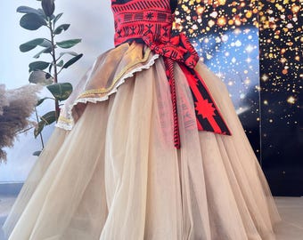 May include: A formal dress with a red and black patterned bodice and a large red bow. The skirt is a layered beige tulle. The dress is displayed on a mannequin. The dress is suitable for a special occasion.
