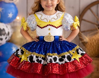 May include: A dress featuring a white bodice with a yellow yoke, puffed sleeves, and a blue sequined skirt with a cow-print band, red sequin trim, and a tulle hem. The dress includes a blue belt with a gold buckle and yellow bows on the sleeves.