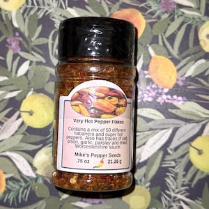 May include: A clear spice jar with a black lid, filled with red pepper flakes. The label reads "Very Hot Pepper Flakes" and "Mike's Pepper Seeds". The jar contains 0.75 oz or 21.26 g of flakes, a mix of habanero and super hot peppers.