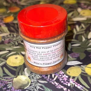May include: A clear jar of Very Hot Pepper Powder with a bright red lid. The label lists ingredients including habanero and super hot peppers, garlic, and Worcestershire sauce. The text "Mike's Pepper Seeds" is also visible.