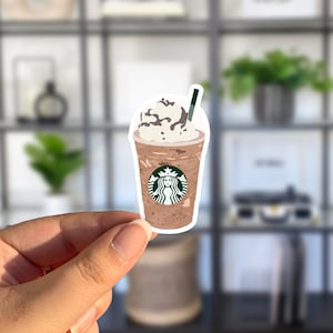May include: A sticker of a brown and white iced coffee drink with whipped cream and chocolate drizzle. The drink has the Starbucks logo on the side and a green straw.