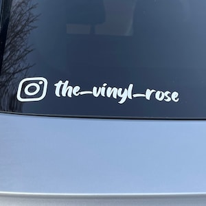 K&ouml;nnte beinhalten: Wei&szlig;er Vinyl-Aufkleber mit einem Instagram-Logo und dem Text "the-vinyl-rose" auf einer grauen Autot&uuml;r.