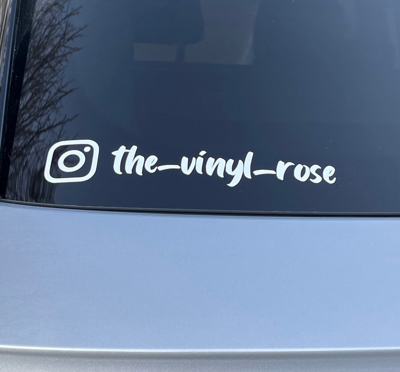 K&ouml;nnte beinhalten: Wei&szlig;er Vinyl-Aufkleber mit einem Instagram-Logo und dem Text "the-vinyl-rose" auf einer grauen Autot&uuml;r.