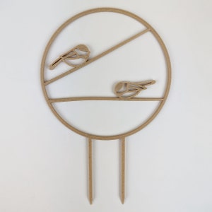 The chickadee trellis. A circle with two legs on the bottom for stakes. Across the middle are two branches running horizontally one on top of the other, each with a chickadee on it. Wood colour against a white background.