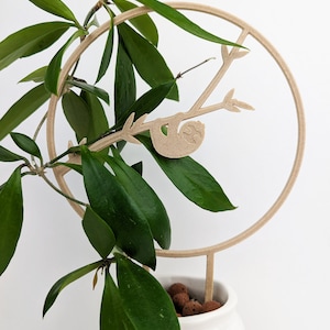 May include: A wooden plant stand with a circular hoop and a sloth hanging from a branch. The stand is designed to support a houseplant.