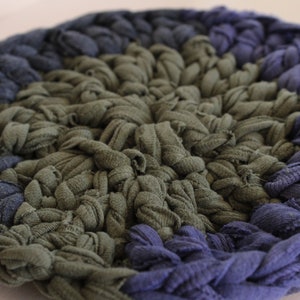 May include: A round, crocheted rug with a center of dark green fabric and a border of dark blue fabric.