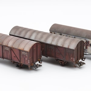 Puede incluir: Tres vagones de tren en miniatura, dos son marrones con un aspecto oxidado y uno es blanco con letras rojas que dicen "Offbrau" y "Rail 1349".