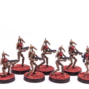 May include: A group of seven tan and red robotic soldier figurines, each holding a black blaster rifle and standing on a textured red base. A single red and white marbled six-sided die with the number one visible is positioned to the left.