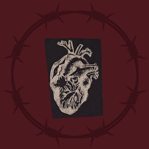 Puede incluir: Un parche de tela negro con una ilustración anatómica de un corazón en blanco y negro.