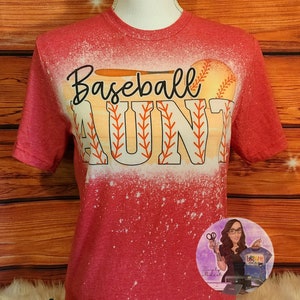 May include: Red t-shirt with a bleach-splattered design featuring a baseball bat and the words "Baseball Aunt".