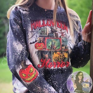 May include: A black sweatshirt with a white splatter design. The sweatshirt has a graphic print of a pumpkin and the text "Halloween Horror Nights".