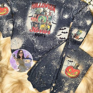 May include: A black and gray sweatshirt and sweatpants set with a bleach-splattered design. The sweatshirt features a graphic of a television screen with a spooky Halloween scene and the text "Halloween Horror Nights". The sweatpants feature a graphic of a jack-o'-lantern.