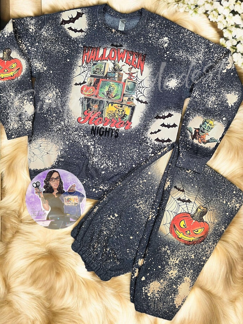 May include: A black and gray sweatshirt and sweatpants set with a bleach-splattered design. The sweatshirt features a graphic of a television screen with a spooky Halloween scene and the text "Halloween Horror Nights". The sweatpants feature a graphic of a jack-o'-lantern.