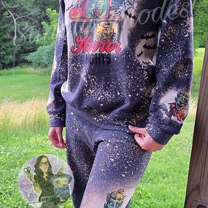 May include: A black and white bleached sweatshirt with a graphic print of a television screen with a horror movie playing. The text "Halloween Horror 1978" is printed below the television. The sweatshirt has a distressed look with white splatter paint.