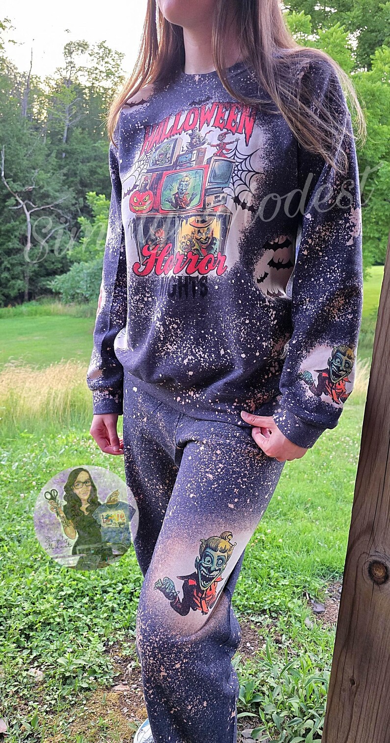 May include: A black and white bleached sweatshirt with a graphic print of a television screen with a horror movie playing. The text "Halloween Horror 1978" is printed below the television. The sweatshirt has a distressed look with white splatter paint.