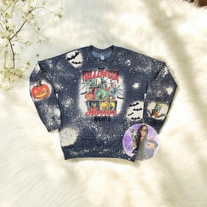 May include: A blue sweatshirt with a bleach-splattered design featuring a vintage television set with a Halloween theme. The text "Halloween Horror Nights" is printed on the sweatshirt.