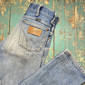 Pode incluir: Jeans Wrangler de ganga azul clara com lavagem desbotada. Os jeans apresentam um patch de couro castanho com o logotipo Wrangler no bolso traseiro. Os jeans t&ecirc;m um design cl&aacute;ssico de cinco bolsos e fecho de bot&atilde;o e z&iacute;per.