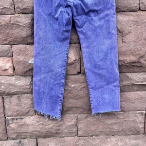 Puede incluir: Unos vaqueros azules con un efecto descolorido. Los vaqueros tienen un corte recto y un dobladillo deshilachado. La mezclilla es azul medio con zonas m&aacute;s claras, lo que indica desgaste y lavado. Los vaqueros son de mezclilla.