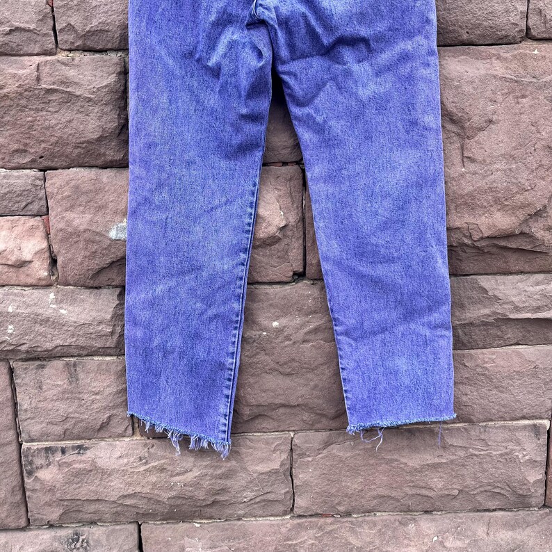 Puede incluir: Unos vaqueros azules con un efecto descolorido. Los vaqueros tienen un corte recto y un dobladillo deshilachado. La mezclilla es azul medio con zonas m&aacute;s claras, lo que indica desgaste y lavado. Los vaqueros son de mezclilla.