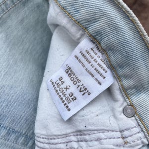May include: Close-up of light blue denim jeans with a white tag. The tag reads "MADE IN MEXICO" and "100% COTTON". The jeans are size 34 x 32 inches.
