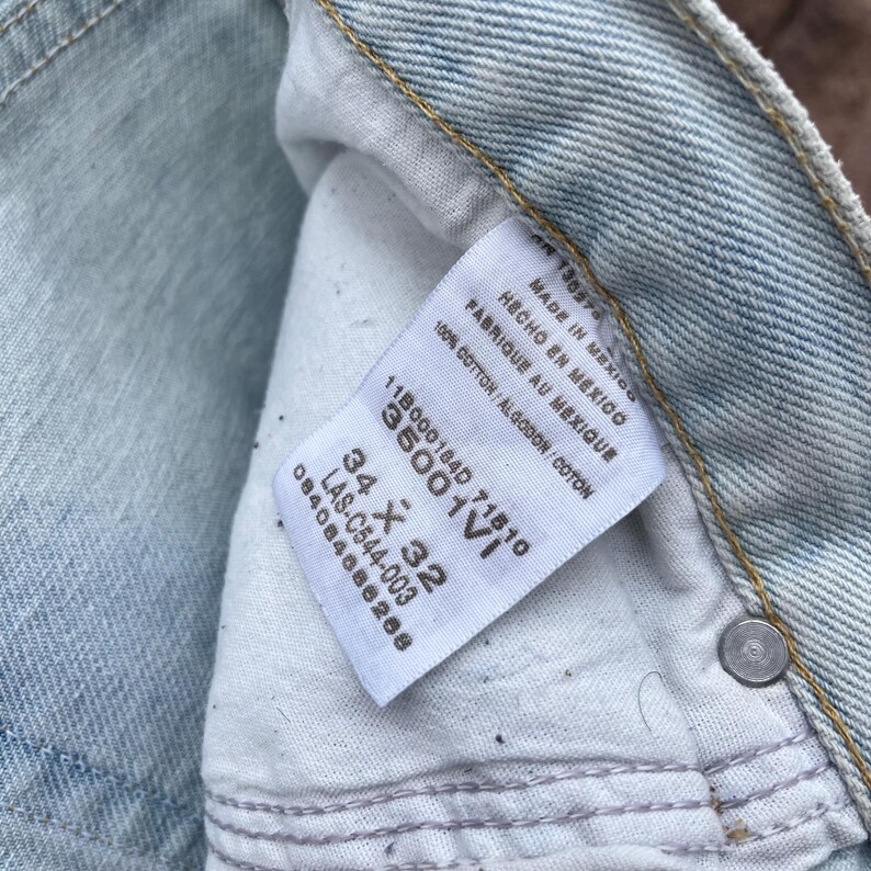 May include: Close-up of light blue denim jeans with a white tag. The tag reads "MADE IN MEXICO" and "100% COTTON". The jeans are size 34 x 32 inches.