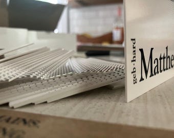 May include: A pile of white business cards with a perforated pattern. The cards feature the name "Matthew" in black, with "geb.hard" printed vertically. The cards are stacked on a wooden surface.