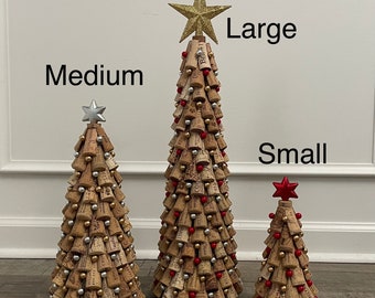 May include: Three cone-shaped trees constructed from wine corks, labeled Medium, Large, and Small. Each tree is decorated with small red, silver, and gold spherical ornaments. The Large tree has a gold star, the Medium has a silver star, and the Small has a red star topper.