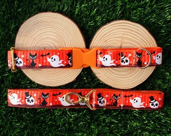 May include: Orange Halloween-themed dog collar and leash set. The collar and leash feature a repeating pattern of white ghosts, black cats, and skull designs on a striped background. The set includes an orange plastic buckle and gold-colored metal hardware.