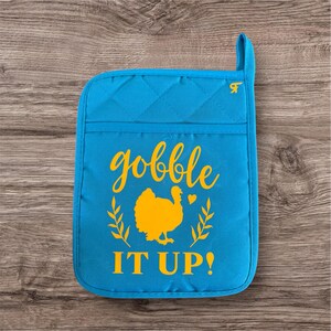 May include: Blue quilted oven mitt with a yellow graphic of a turkey and the text "gobble it up!"